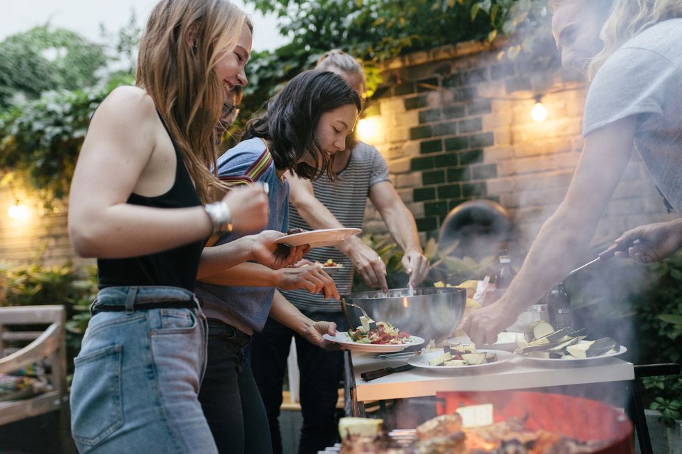 a young group of friends are helping themselves to freshly prepared food at a summer evening barbecue