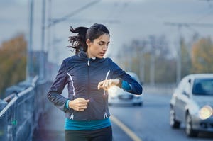 young fitness woman runner checking time from smart watch young woman checking heart rate while jogging on street at dusk young woman looking on smartwatch her heartbeat while running in city r