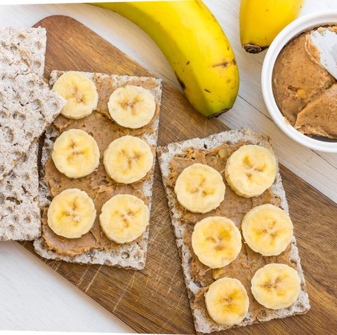 Healthy vegan snack with scandinavian rye crispbread, homemade peanut butter and slices of Canary island bananas bananas, wood cutting board, top view