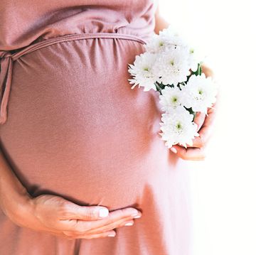 Pregnant woman with chrysanthemums flowers holds hands on belly at white background.