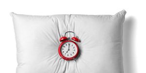 close up of a white pillow and red alarm clockon white background