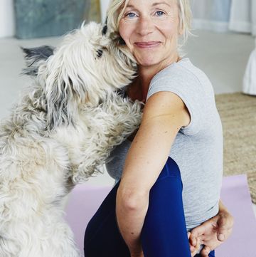 happy senior woman sitting on a yoga mat trying to do her exercise and being distracted by her fluffy dog