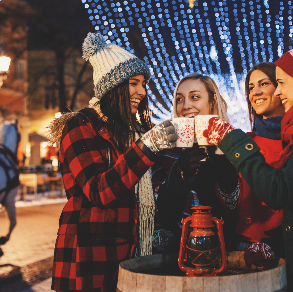 group of friends enjoying the magic of christmas by cheering with mulled wine and hot tea on a street at a city decorated with christmas lights