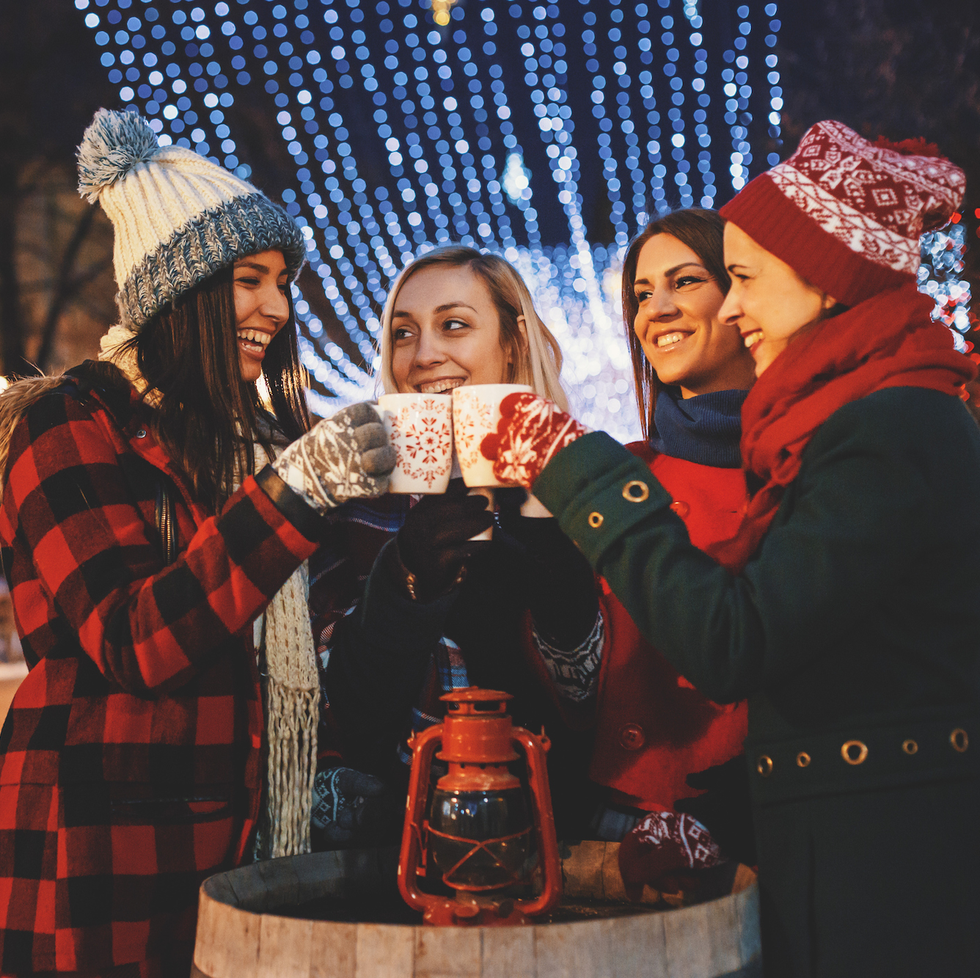 group of friends enjoying the magic of christmas by cheering with mulled wine and hot tea on a street at a city decorated with christmas lights