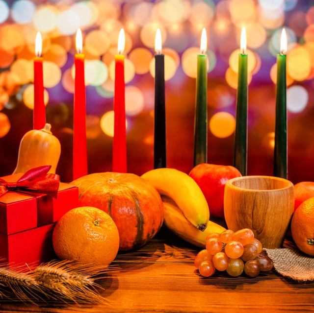 kwanzaa holiday concept with decorate seven candles red, black and green, gift box, pumpkin, bowl and fruit on light blur bokeh background