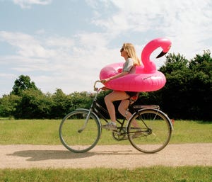 young woman cycling though park with pink flamingo swim ring