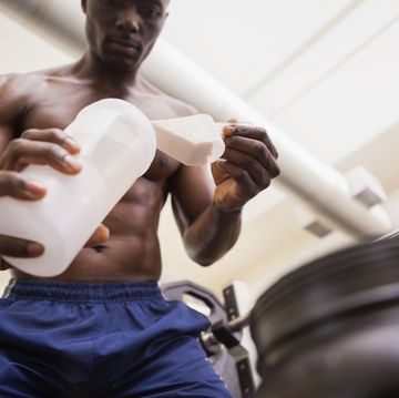 shirtless body builder scooping up protein powder in gym