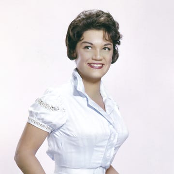 a woman in a white short sleeve dress with a collar smiles as she looks up to the left