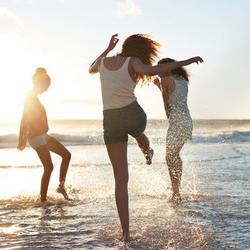 Three young women kicking water and laughing on the beach young women hanging out at the beach, at sunset
