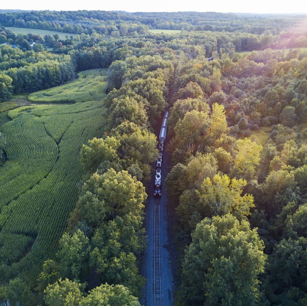 a drone aerial view of a freight and passenger train going through a countryside on a late summer evening
