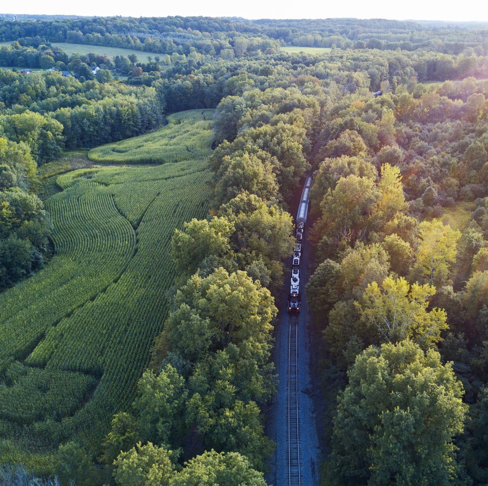 a drone aerial view of a freight and passenger train going through a countryside on a late summer evening