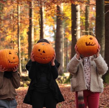 two girls and a boy are playing halloween in the woods, covering their faces with carved pumpkins