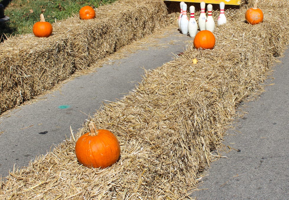bales of hay on a driveway with pumpkins on top and bowling pins at the end