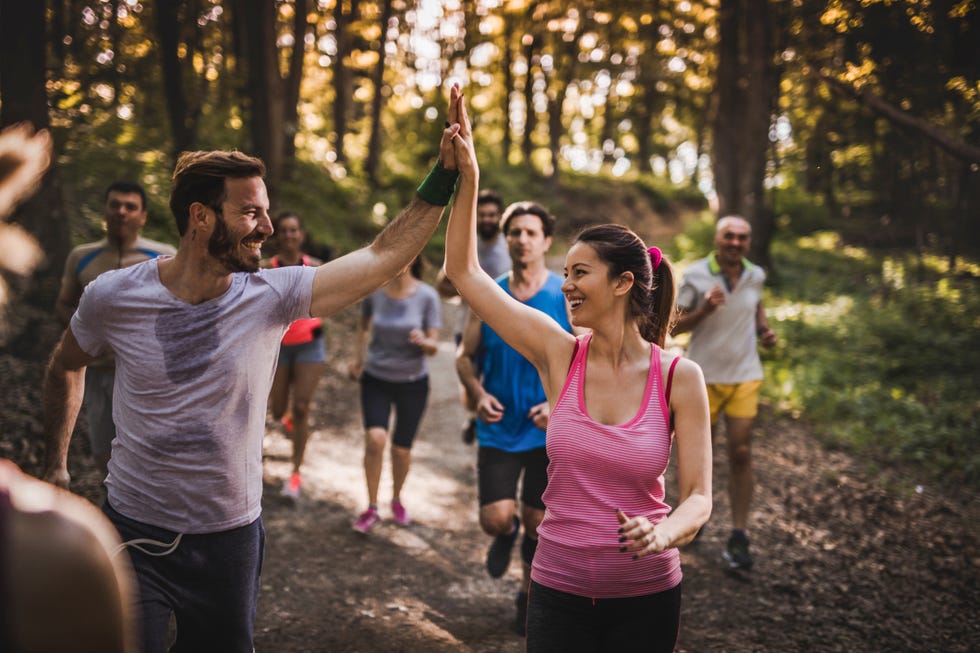 happy marathon runners giving each other high five while running a race in the forest