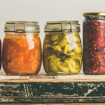 autumn seasonal pickled or fermented vegetables in jars placed in row over vintage kitchen drawer, white wall background, copy space fall home food preserving or canning