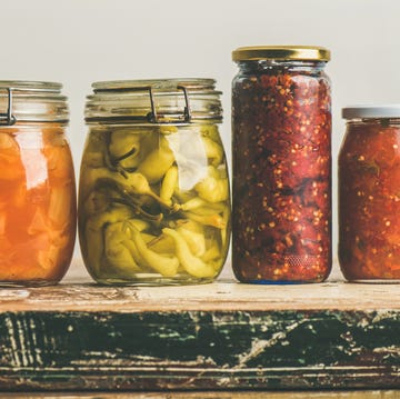 autumn seasonal pickled or fermented vegetables in jars placed in row over vintage kitchen drawer, white wall background, copy space fall home food preserving or canning