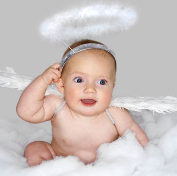 baby dressed as angel with halo and wings of white feathers sitting in white fluff that looks like clouds
