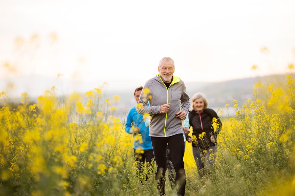 group of active seniors running together outside on the meadow full of flowers front view