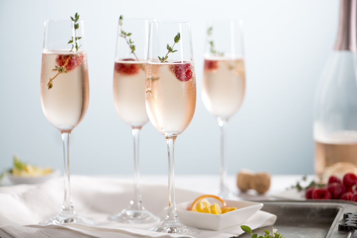 flutes of pink rose champagne garnished with red raspberries and green thyme make for a festive cocktail gathering