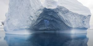 massive blue and green iceberg and reflections, its ice sculpted by waves and melting of ice, floating in calm sea in summer , gerlache passage, antarctica antarctic peninsula southern ocean