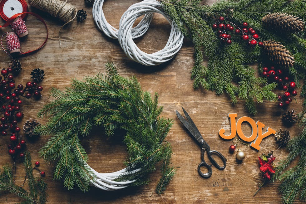 top view of creation of christmas wreaths with fir branches and pine cones on wooden table with word joy and scissors