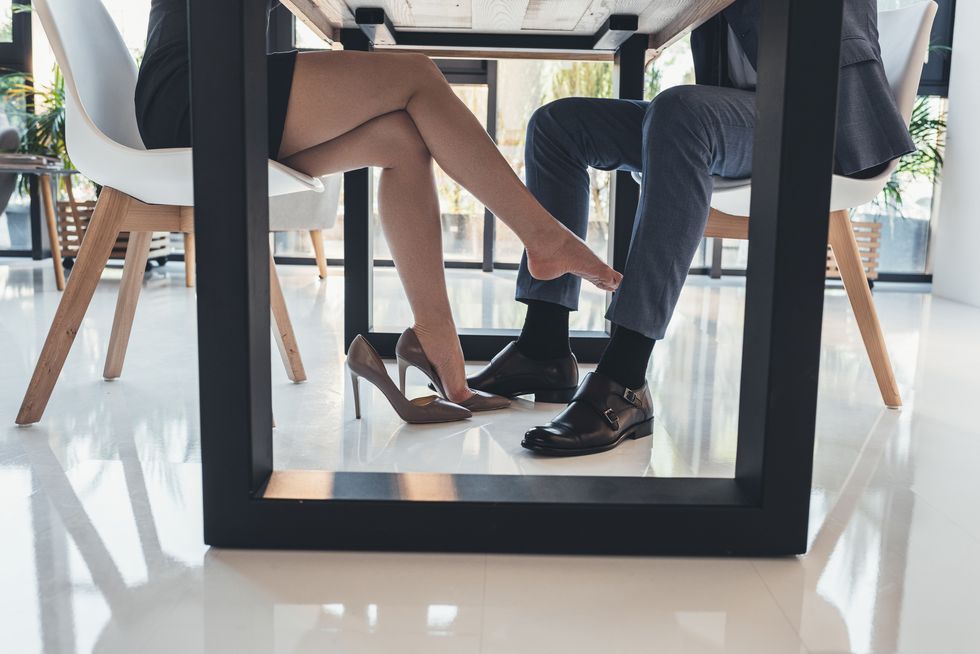 cropped shot of a woman flirtatiously touching leg of man in a suit with her foot under the table