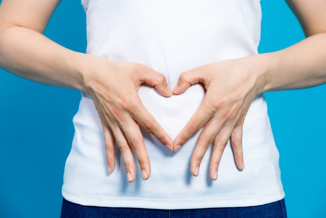 young woman who makes a heart shape by hands on her stomach