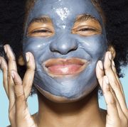 close up of young mixed race woman applying blue cleansing face mask on her face,  with turquoise background
