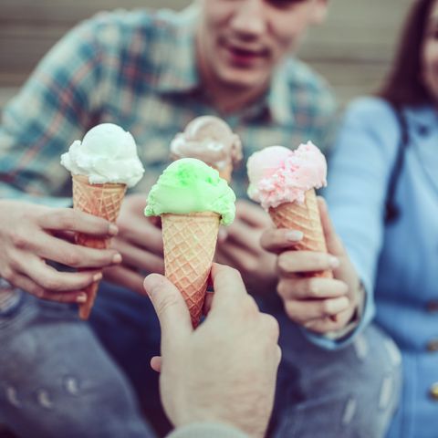 smiling teenage friends eating ice cream and holding cones in hands