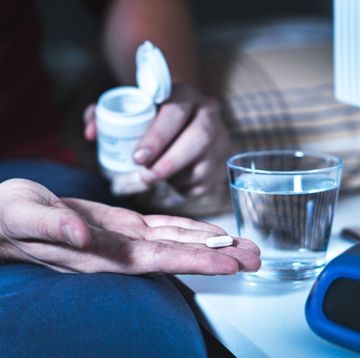 man's hand holding pill, man sitting on bed
