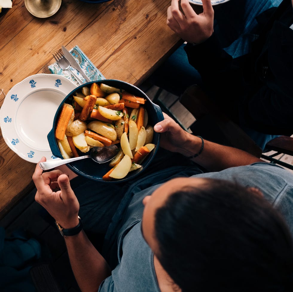 High angle view of man holding utensil of potatoes and carrots while sitting with friends