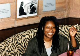 actress whoopi goldberg at a table with a cigarette in her hand