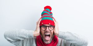 christmas portrait of angry nerdy man wearing elf cap and red scarf man wearing winter sweater covering his ears against white background