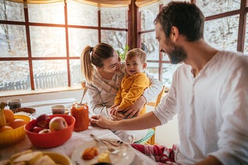 portrait of a cheerful young family having breakfast in their cottage house on the countryside, while it is snowing outside