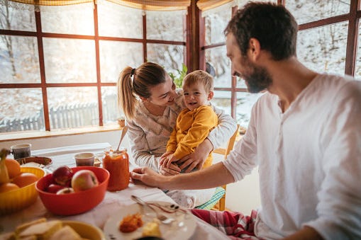 portrait of a cheerful young family having breakfast in their cottage house on the countryside, while it is snowing outside