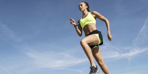 Low angle view of young female runner running along sea wall against blue sky