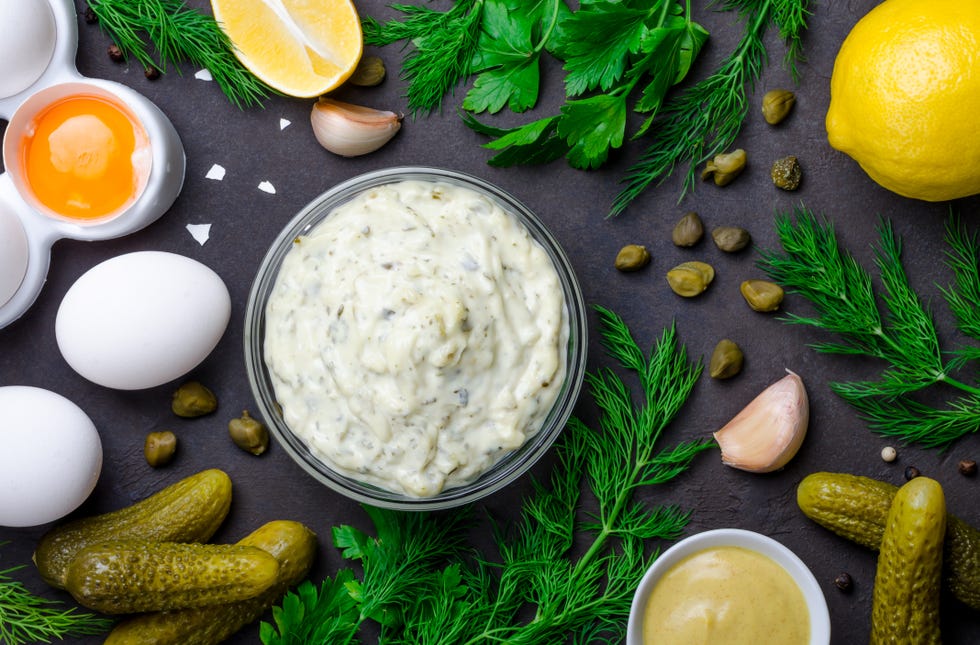 ways to use pickle juice homemade tartar tartare with ingredients pickles, capers, dill, parsley, garlic, lemon and mustard on a dark black stone concrete background horizontal top view
