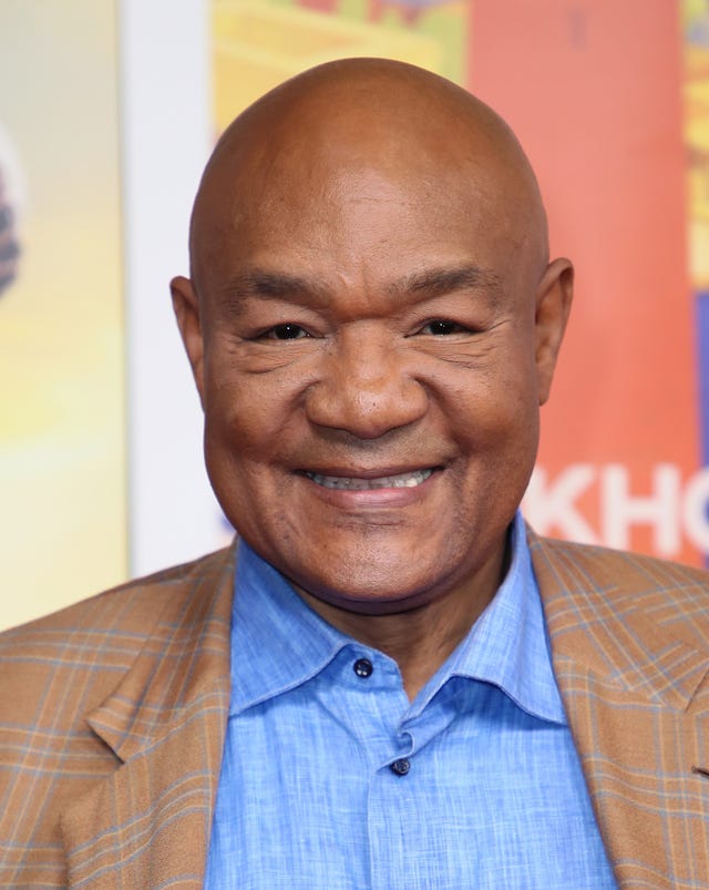 george foreman smiles at the camera, he wears a brown and blue plaid suit jacket and a blue collared shirt (photo by david livingston/getty images)