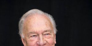 christopher plummer smiles and looks right of the camera, he wears a brown plaid suit jacket over a blue collared shirt