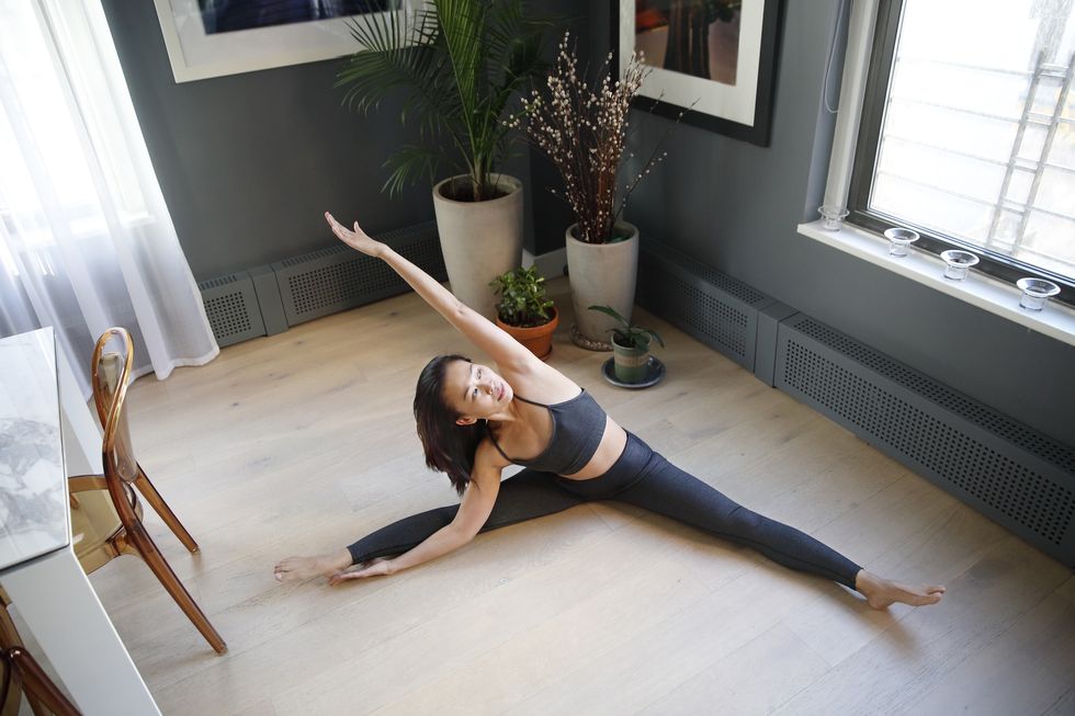 fit asian woman stretching in a yoga pose seen from above, in a modern apartment setting