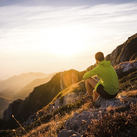 Italy, mountain running man sitting on rock looking at sunset