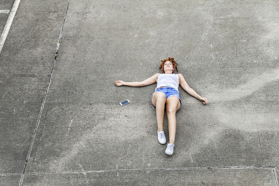 young woman lying on parking level next to cell phone