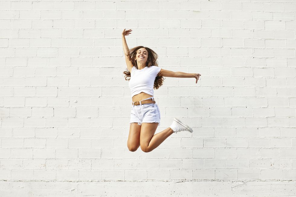Happy young woman jumping mid-air in front of white wall