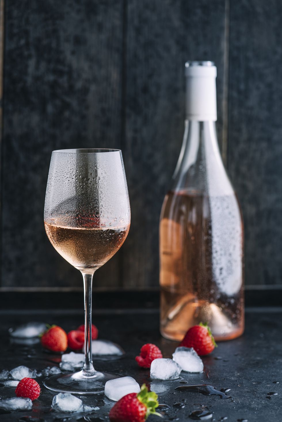 rosé wine with ice cubes and fruits as aroma symbols on dark background