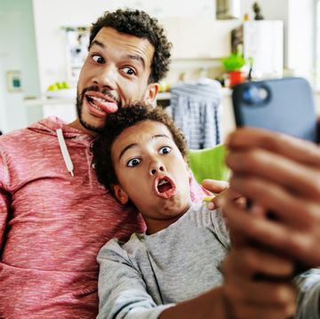 a father and son at home pulling silly faces while taking a selfie together on a smartphone