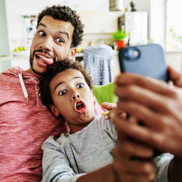 a father and son at home pulling silly faces while taking a selfie together on a smartphone