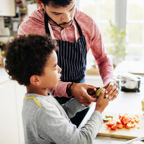 a father is carefully showing his son how to peel fruit and chop vegetables at home in the kitchen