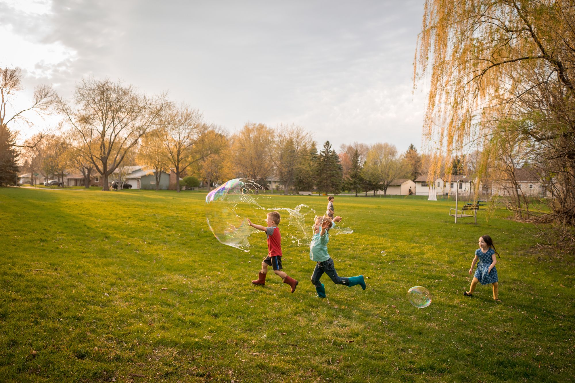 four children chasing giant soap bubbles in a public park