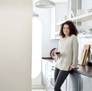 Woman smiling at camera relaxing in kitchen with a glass of wine