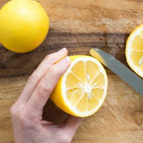 Cropped Image Of Hand Cutting Lemon On Cutting Board
